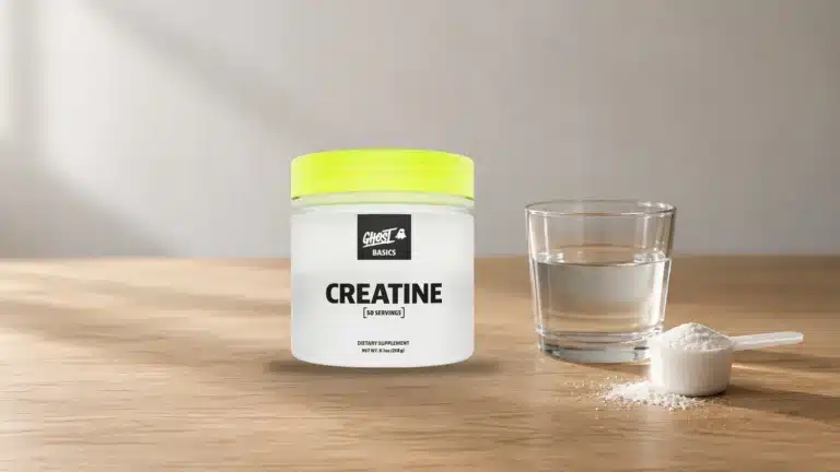 Bote de creatina junto a un vaso de agua y una cuchara medidora